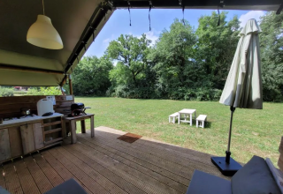Vista da una terrazza in legno con cucina esterna su prato verde e tavolo da picnic in campeggio soleggiato.