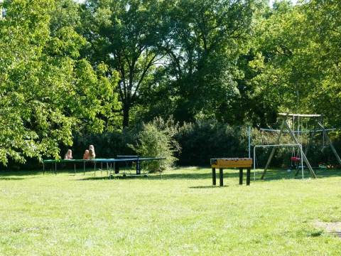 Area giochi all’aperto al campeggio Mas du Midi in Occitania, Francia, con calcetto e altalene verdi.