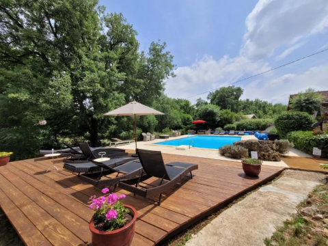 Area piscina all'aperto con lettini, ombrellone e terrazza in legno al Campeggio Mas du Midi in Occitania, Francia.