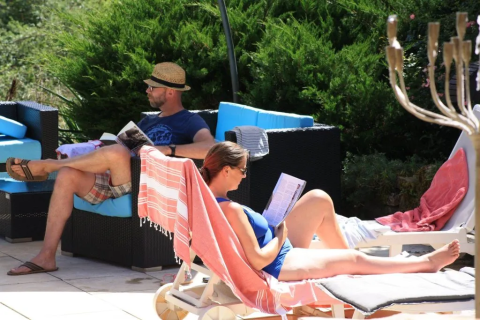 Due persone si rilassano leggendo a bordo piscina al Mas du Midi, parco vacanze in Occitania, Francia.