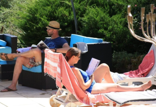 Due persone si rilassano leggendo a bordo piscina al Mas du Midi, parco vacanze in Occitania, Francia.