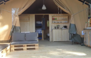 Interno di una tenda safari con divano, angolo cottura e mobili in legno al campeggio Mas du Midi in Francia.