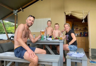 Famille profitant d’un moment devant une tente safari au camping Mas du Midi en France, autour d’une table.