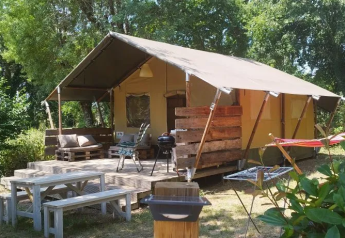 Tenda safari al Campeggio Mas du Midi in Francia, con area picnic, tavolo e barbecue immersi nella natura.