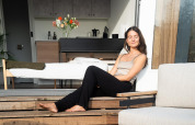 Femme profitant du soleil sur la terrasse d’un lodge moderne, avec des fleurs à l’intérieur.
