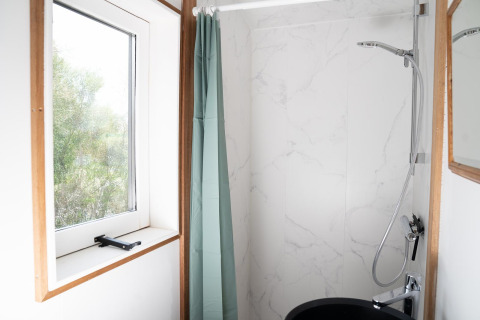 Baño luminoso con ventana, cortina de ducha verde y ducha moderna en Slowcabin Nest en Zomerlicht, Países Bajos.