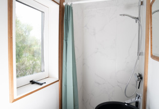 Baño luminoso con ventana, cortina de ducha verde y ducha moderna en Slowcabin Nest en Zomerlicht, Países Bajos.