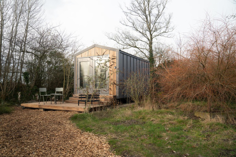 Cabaña Slowcabin Nest en un bosque tranquilo, con terraza de madera, sillas y puerta de cristal.