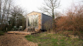 Lodge Slowcabin Nest en forêt paisible, avec terrasse en bois, chaises et entrée vitrée moderne.