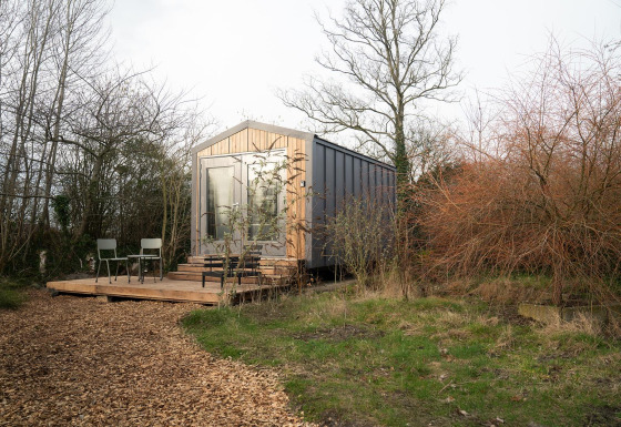 Cabaña Slowcabin Nest en un bosque tranquilo, con terraza de madera, sillas y puerta de cristal.