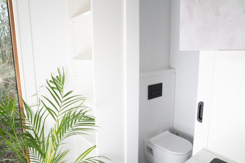 Inodoro moderno y minimalista en Slowcabin Nest en Zomerlicht, Países Bajos, con paredes blancas y planta verde.