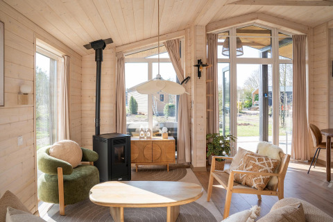 Lichte, moderne woonkamer in Slowlodge bij Zomerlicht, Nederland, met grote ramen en knusse inrichting.