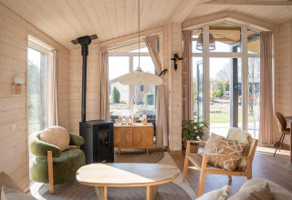 Lichte, moderne woonkamer in Slowlodge bij Zomerlicht, Nederland, met grote ramen en knusse inrichting.