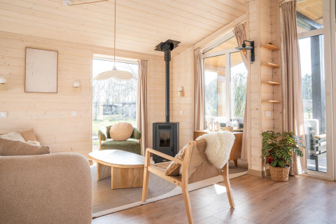 Lichte, gezellige woonkamer in de Slowlodge bij Zomerlicht, Nederland, met houten interieur en grote ramen.