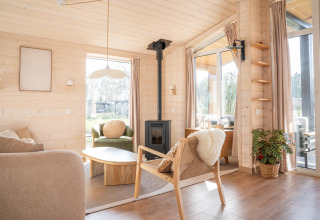 Lichte, gezellige woonkamer in de Slowlodge bij Zomerlicht, Nederland, met houten interieur en grote ramen.