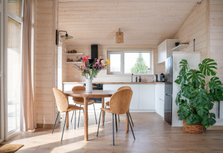 Lichte, moderne keuken en eetruimte met houten wanden, grote plant en bloemen bij Slowlodge, Zomerlicht, Nederland.