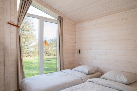 Lichte slaapkamer met twee eenpersoonsbedden en grote ramen in Slowlodge, Zomerlicht in Nederland.