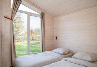 Lichte slaapkamer met twee eenpersoonsbedden en grote ramen in Slowlodge, Zomerlicht in Nederland.