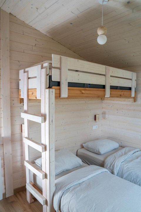 Lichte houten kamer in Slowlodge, Zomerlicht Nederland, met een stapelbed en twee eenpersoonsbedden.
