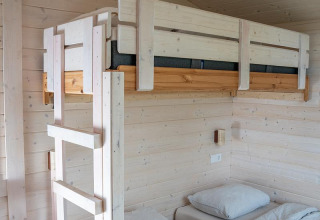 Lichte houten kamer in Slowlodge, Zomerlicht Nederland, met een stapelbed en twee eenpersoonsbedden.