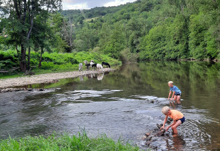Due bambini giocano in un fiume poco profondo con cavalli al pascolo vicino al campeggio La Prade in Francia.