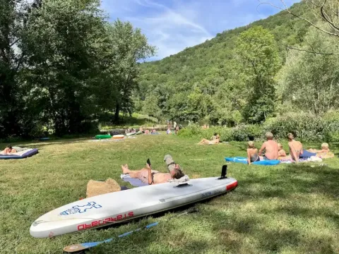 Villeggianti sdraiati sull’erba al campeggio La Prade in Occitania, Francia, immersi nella natura verde.