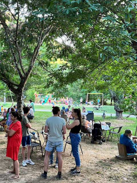 Persone si rilassano in un campeggio in Francia con bambini che giocano su un parco giochi colorato sullo sfondo.