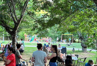 Persone si rilassano in un campeggio in Francia con bambini che giocano su un parco giochi colorato sullo sfondo.