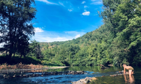 Persona che gioca in un fiume poco profondo circondata da alberi verdi al Camping La Prade in Occitania.
