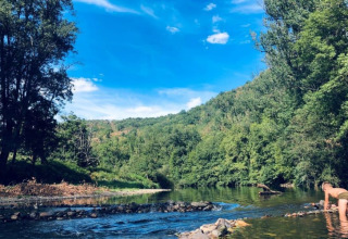 Persona che gioca in un fiume poco profondo circondata da alberi verdi al Camping La Prade in Occitania.