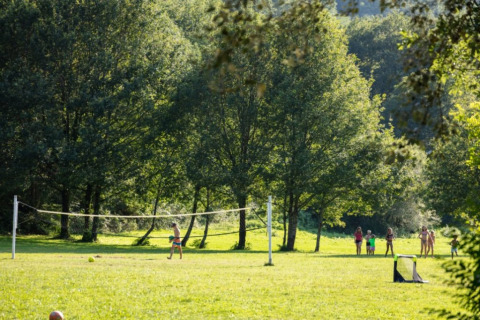 Bambini che giocano vicino a una rete da pallavolo nel parco soleggiato del campeggio La Prade in Occitanie.