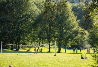 Bambini che giocano vicino a una rete da pallavolo nel parco soleggiato del campeggio La Prade in Occitanie.