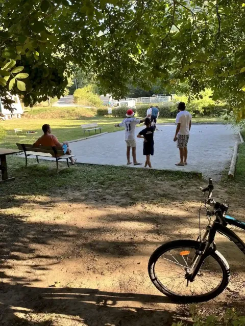 Persone giocano all'aperto al campeggio La Prade in Occitania, Francia, con una bici in primo piano.