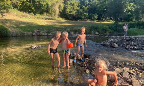 Bambini giocano in un fiume poco profondo al campeggio La Prade, Occitania, Francia, immersi nel verde.