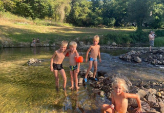 Bambini giocano in un fiume poco profondo al campeggio La Prade, Occitania, Francia, immersi nel verde.