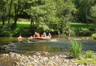 Persone si divertono in un fiume poco profondo vicino al campeggio La Prade in Occitania, Francia, circondate dal verde.