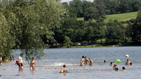 Persone si godono una giornata in un lago presso un parco vacanze con glamping e paesaggio verdeggiante.