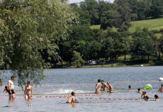 Persone si godono una giornata in un lago presso un parco vacanze con glamping e paesaggio verdeggiante.