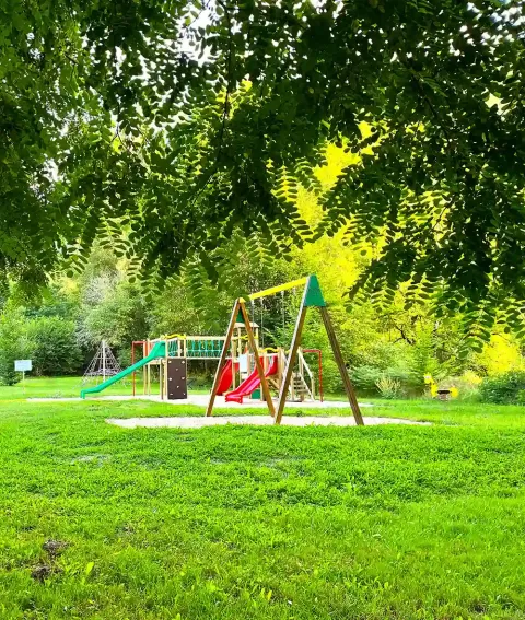 Area giochi per bambini al campeggio La Prade in Occitania, Francia, con altalene e scivoli immersi nel verde.