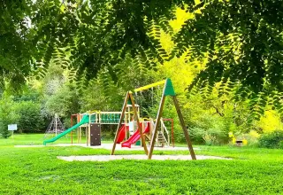 Area giochi per bambini al campeggio La Prade in Occitania, Francia, con altalene e scivoli immersi nel verde.