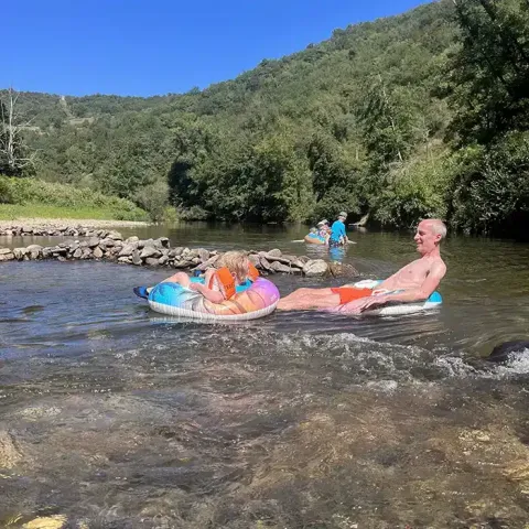 Persone che si rilassano su salvagenti in un fiume circondato da colline al campeggio La Prade, Occitania, Francia.