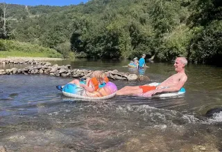 Persone che si rilassano su salvagenti in un fiume circondato da colline al campeggio La Prade, Occitania, Francia.
