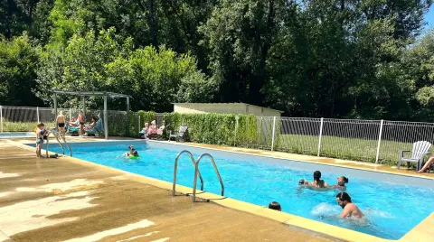 Famiglie nuotano e si rilassano nella piscina all'aperto del campeggio La Prade in Occitania, Francia.