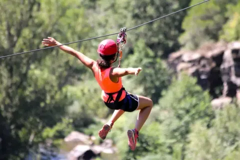 Person fährt an einer Seilrutsche durch Natur, mit Helm und Gurt, während eines Glamping-Urlaubs.
