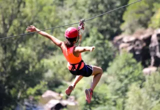 Persona su una zipline nella natura, con casco e imbracatura, in un parco di glamping.