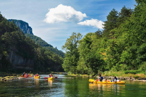 Mensen peddelen in gele kano’s op een rivier omringd door bossen, bij een glamping vakantiepark.