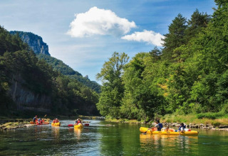 Mensen peddelen in gele kano’s op een rivier omringd door bossen, bij een glamping vakantiepark.