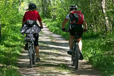 Due persone pedalano lungo un sentiero nel bosco, esperienza comune nei parchi vacanze glamping.