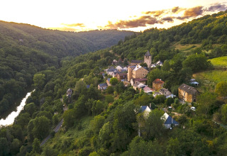 Vista aerea di un villaggio nella valle circondato da verde e sistemazioni glamping in un parco vacanze.