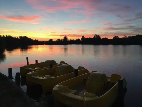 Sunset over a lake with yellow pedal boats at Domaine d'Essendieras holiday park in Nouvelle-Aquitaine, France.